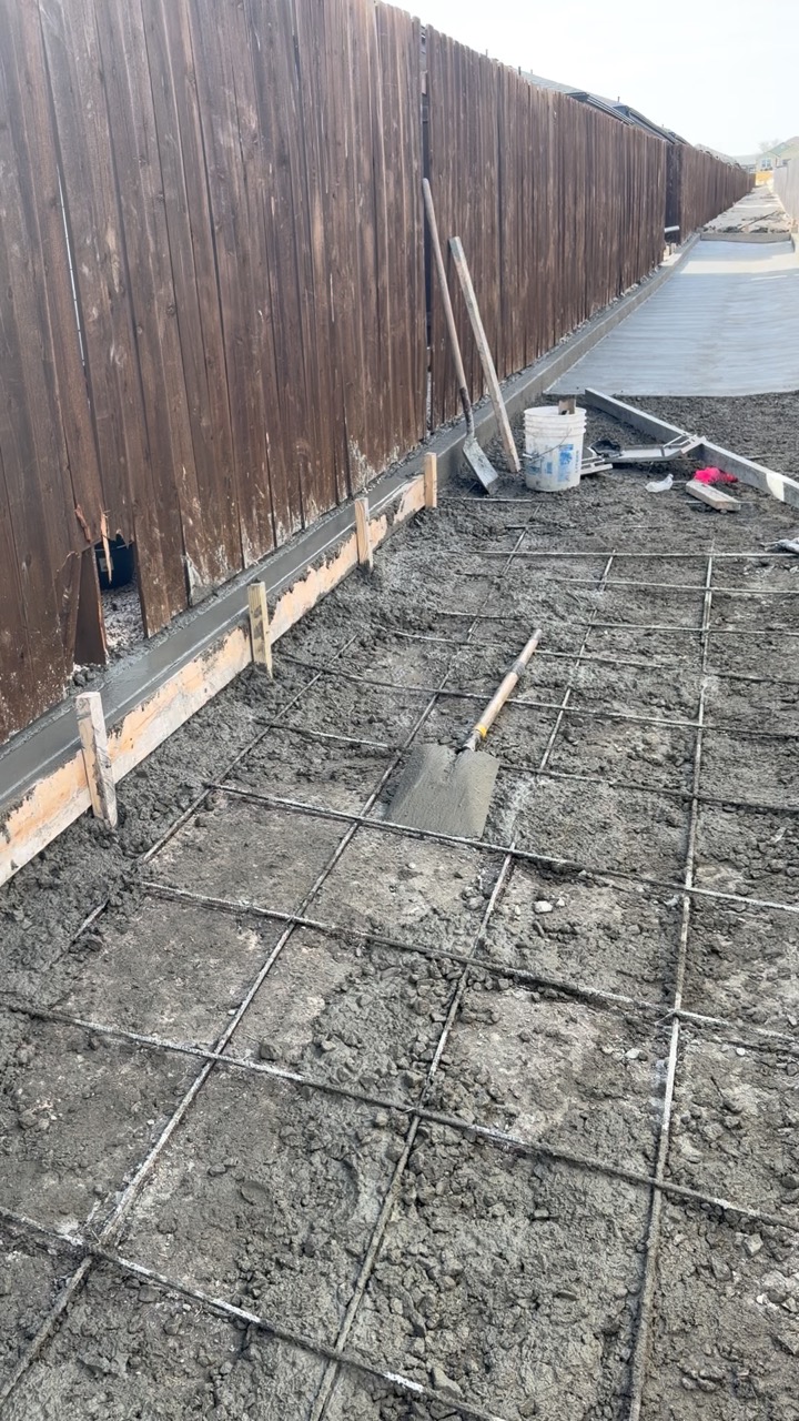 Concrete drainage-channel work along the narrow Temple fence-line corridor
